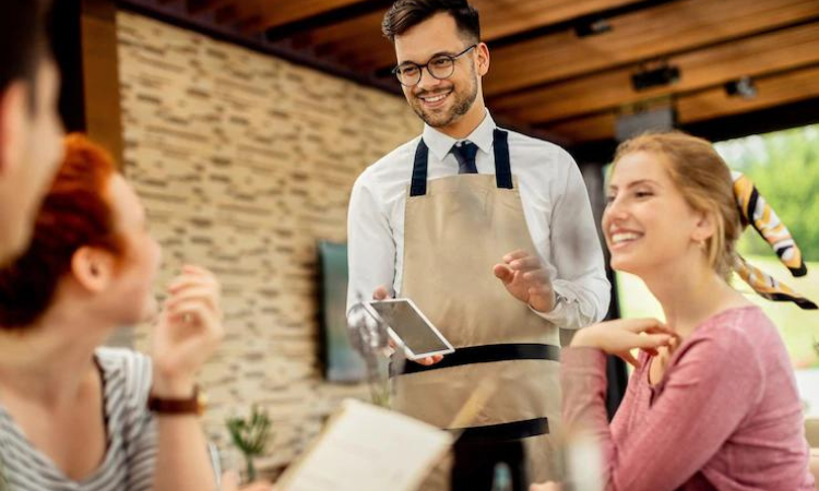 smiling waiter in hotel handing over tablet to guests to utilize the ways hotels should use online survey tool to collect guest feedback